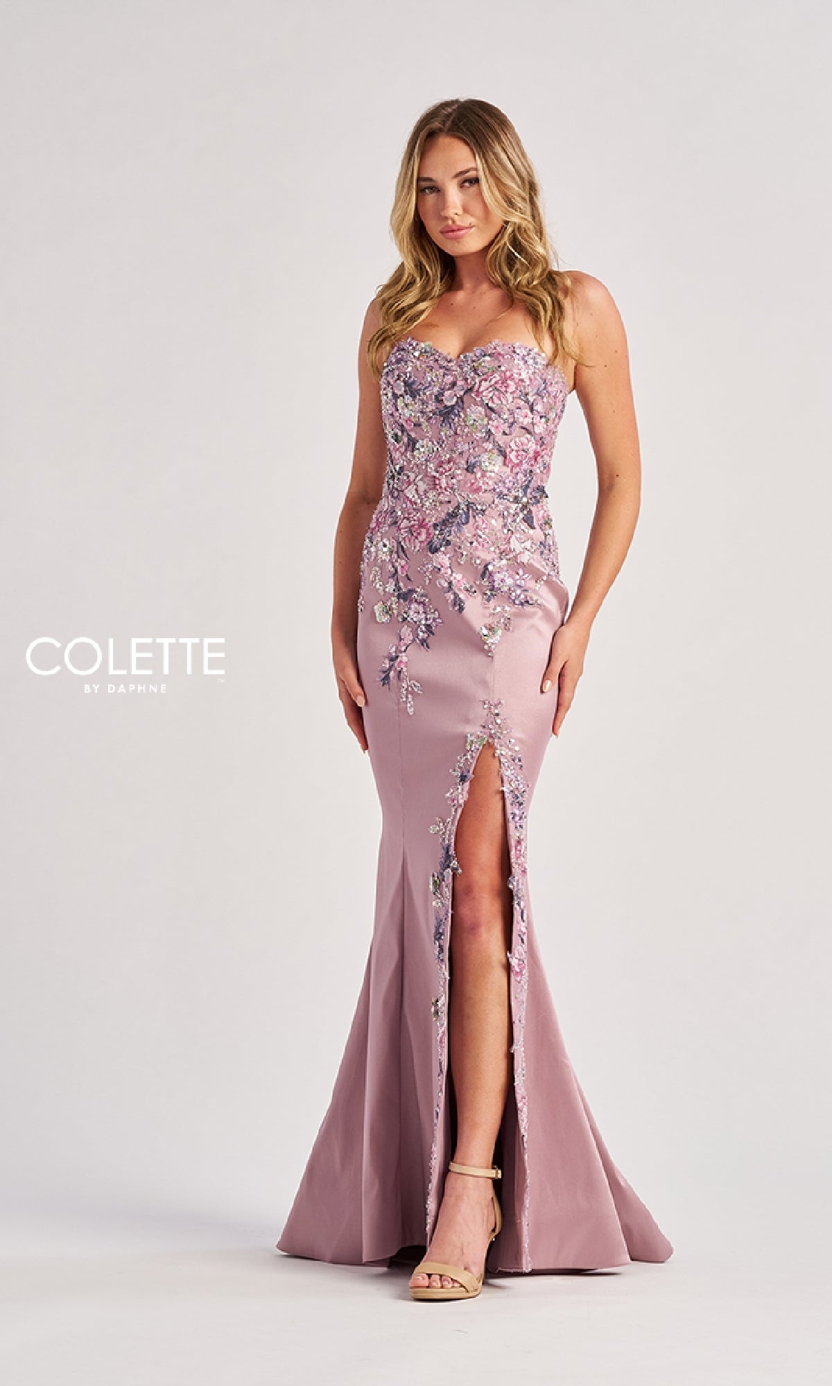 A woman wears the Long Prom Dress: Colette CL8410, a light purple strapless gown with floral embroidery and a front slit, standing against a plain light background.